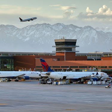 Two Delta airplanes parked at gates, with one plane ascending in front of a mountain backdrop