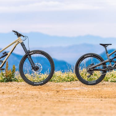 Two bikes stand on a dirt plateau with mountains in the backdrop