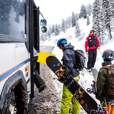 A ski patrol member watches on as snowboarders board the shuttle bus