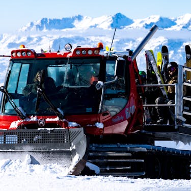 A snowcat carries excited skiers and snowboarders in the back