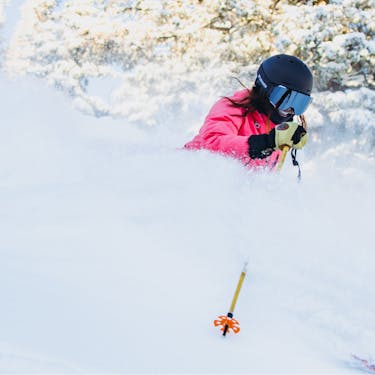 A female skier smiles as she slashes through powder