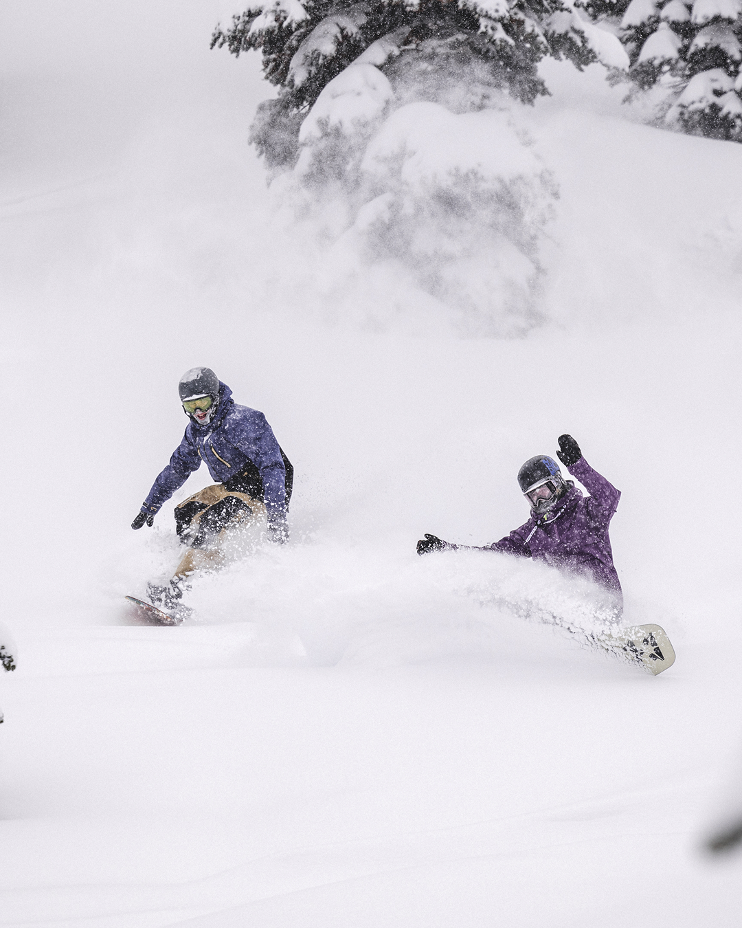 Two snowboarders riding powder