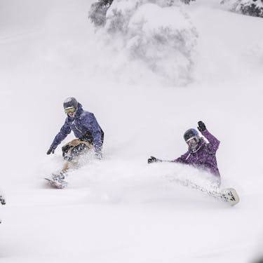 Two snowboarders riding powder