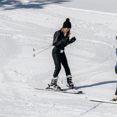 A ski instructor faces a woman and guides her downhill