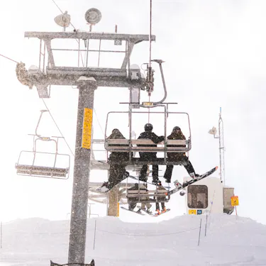 Three snowboarders riding up a lift.
