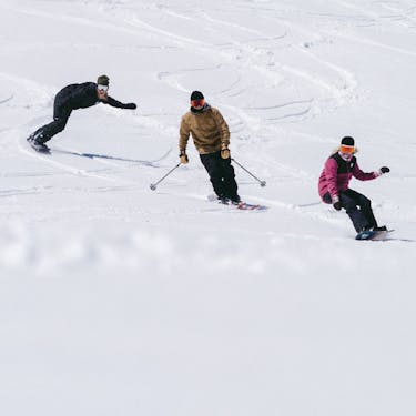 Two snowboarders and a skier ride down the hill together smiling