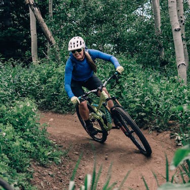 Woman riding mountain bike through forest while smiling