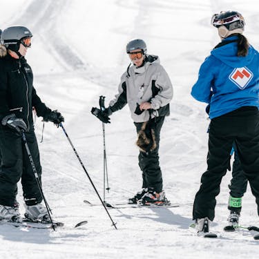 A group of skiers converse with an instructor