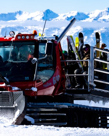 A group of skiers ride in the back of a snowcat