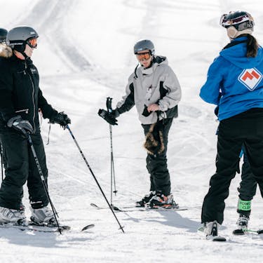 A group of skiers converse with an instructor