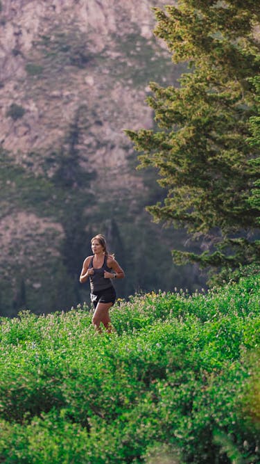 A woman runs through a lush open field with a spectacular mountain view behind her
