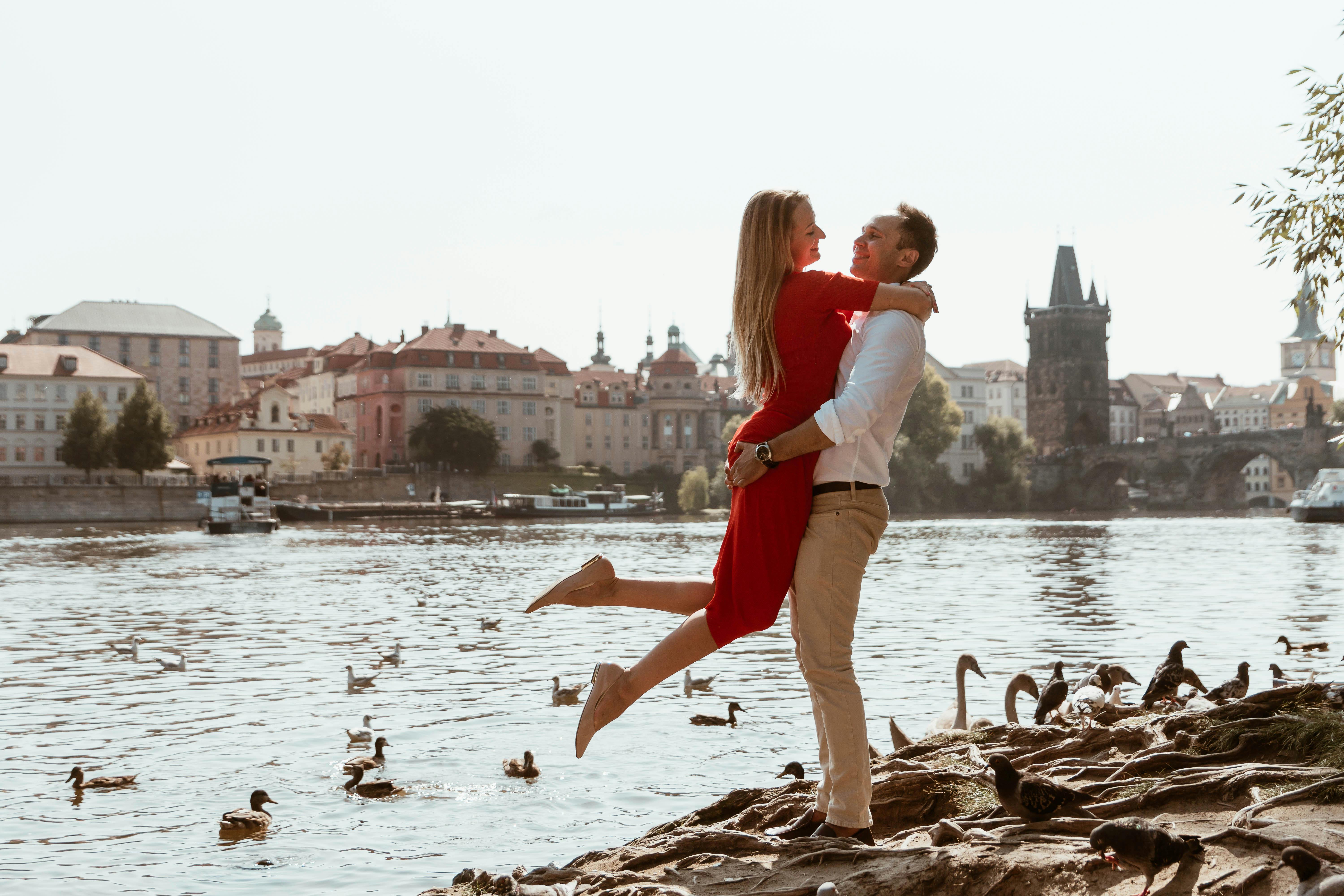 A couple laughing and embracing on the Vltava Riverbank with Prague Castle and swans in the background.