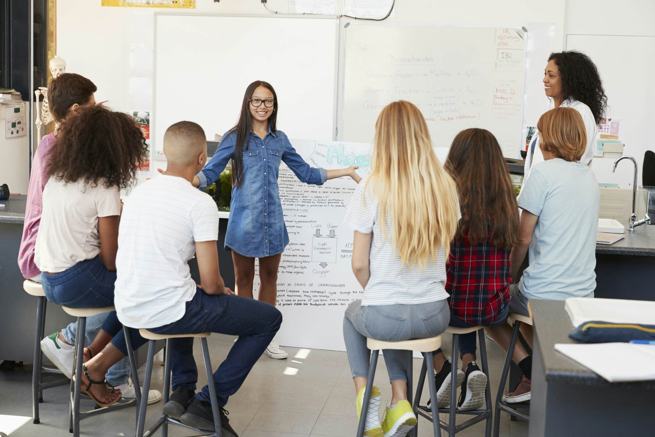 Student presenting her project to a teacher and group of students