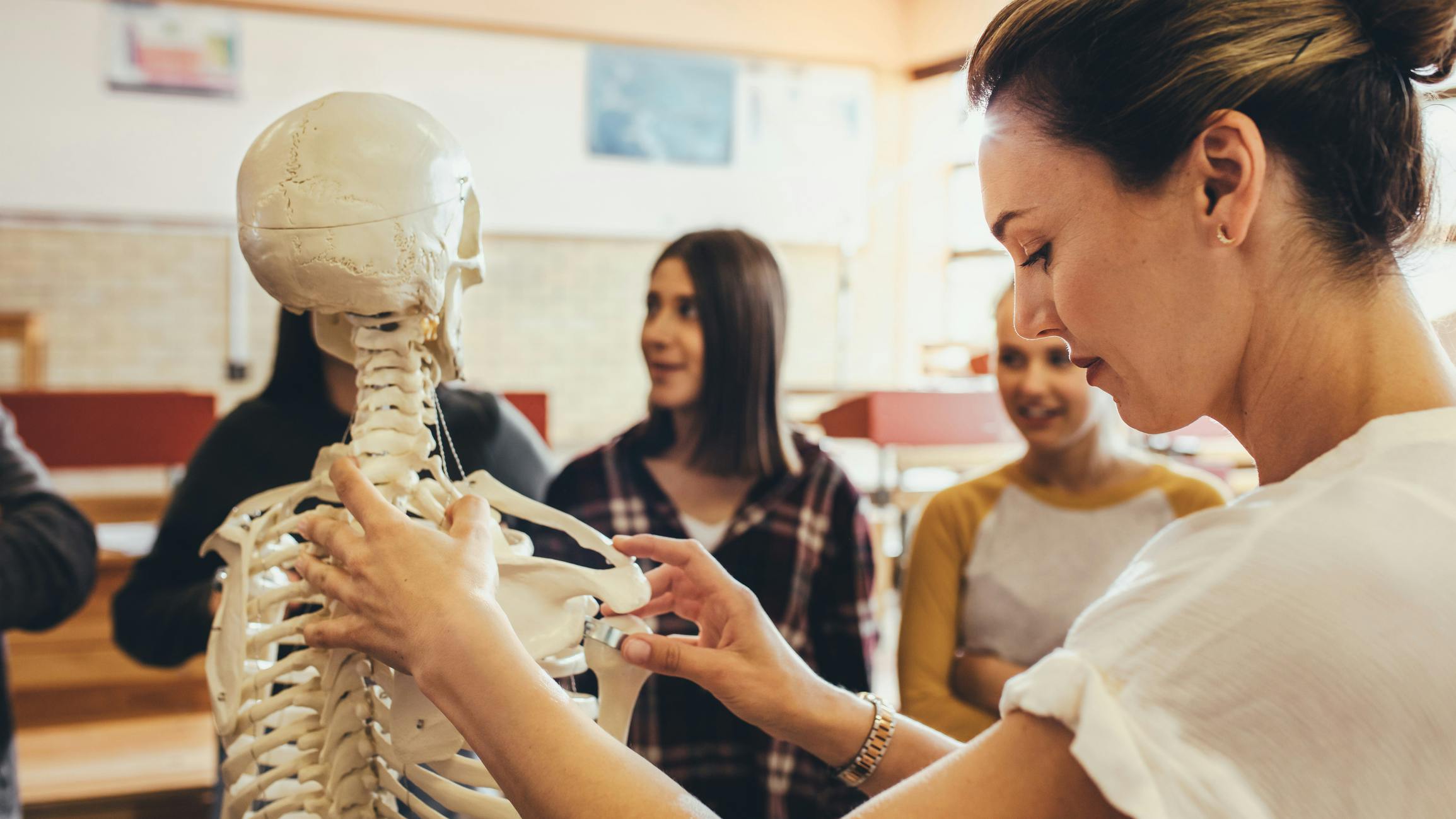 Teacher teaching medicine lesson to high school students on classroom skeleton