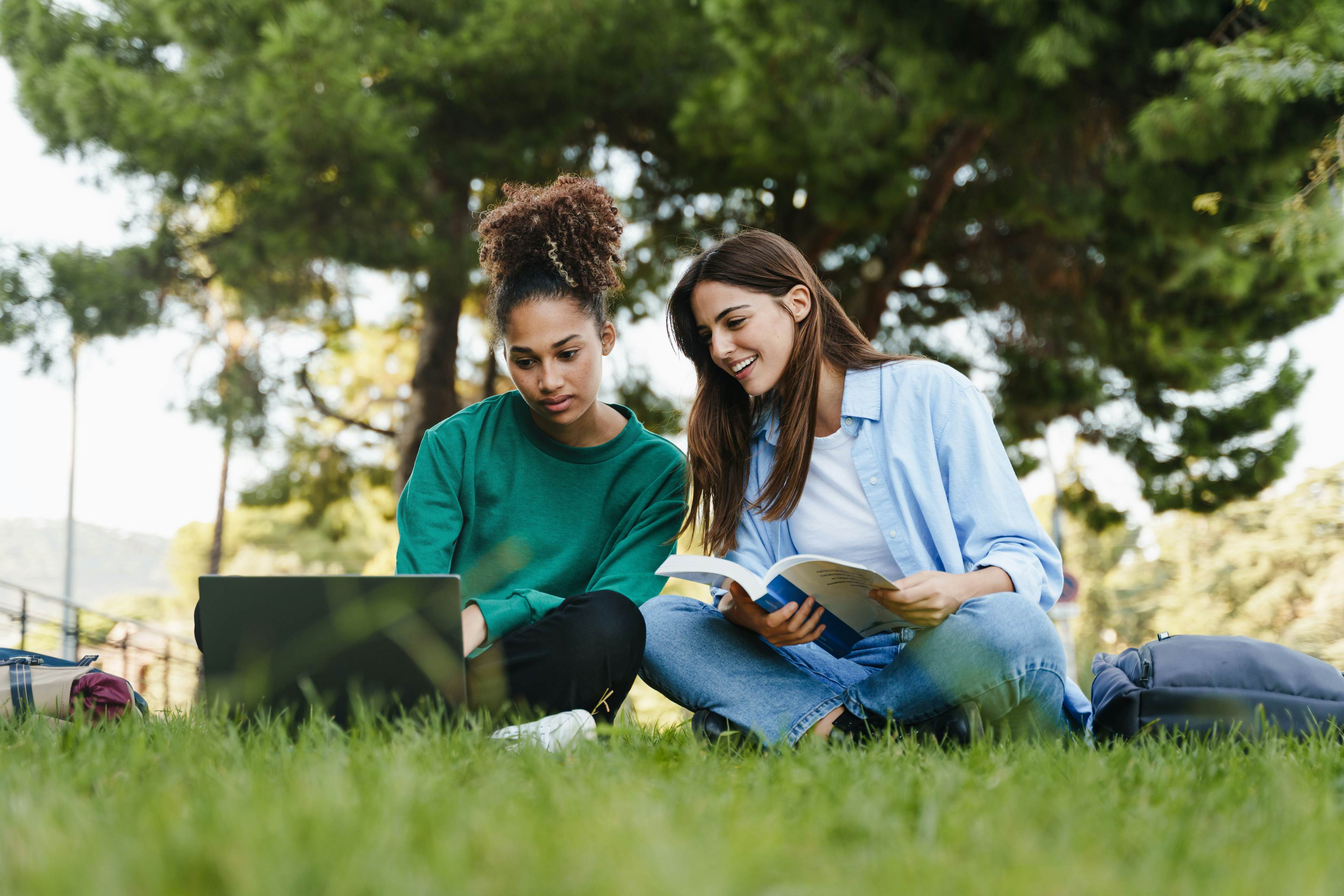 Two female high school students studying on the grass together at a college campus