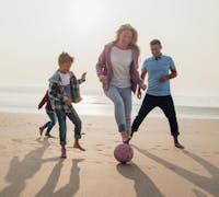 Family playing soccer on the beach.