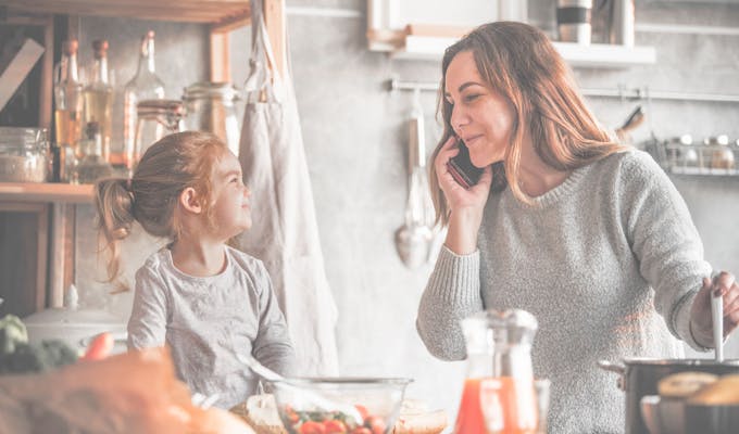 Mom cooking with daughter and talking on phone.
