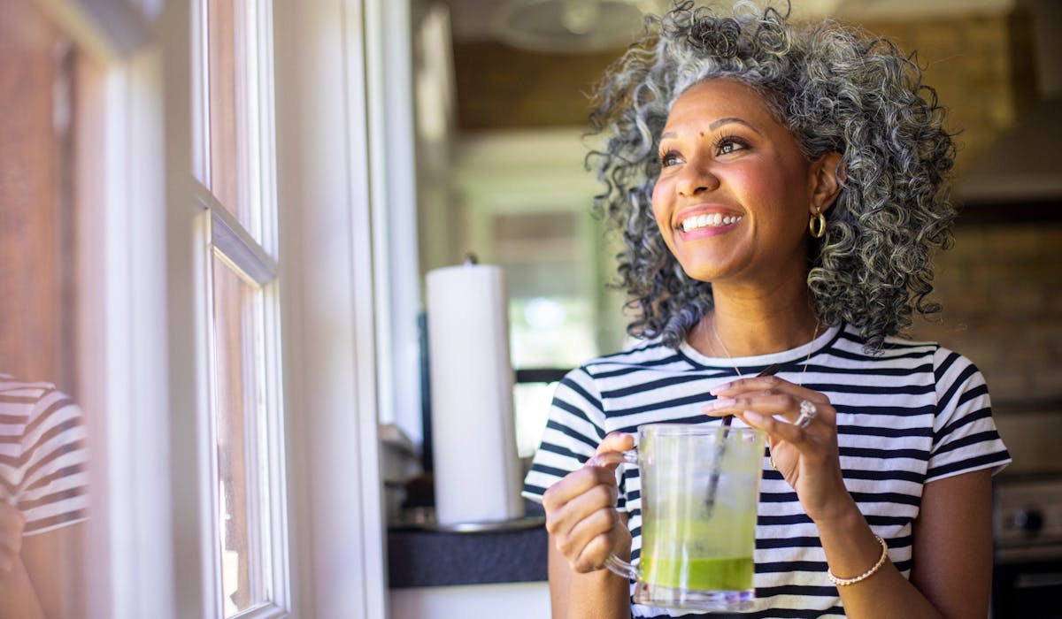 mature woman drinking green juice near window