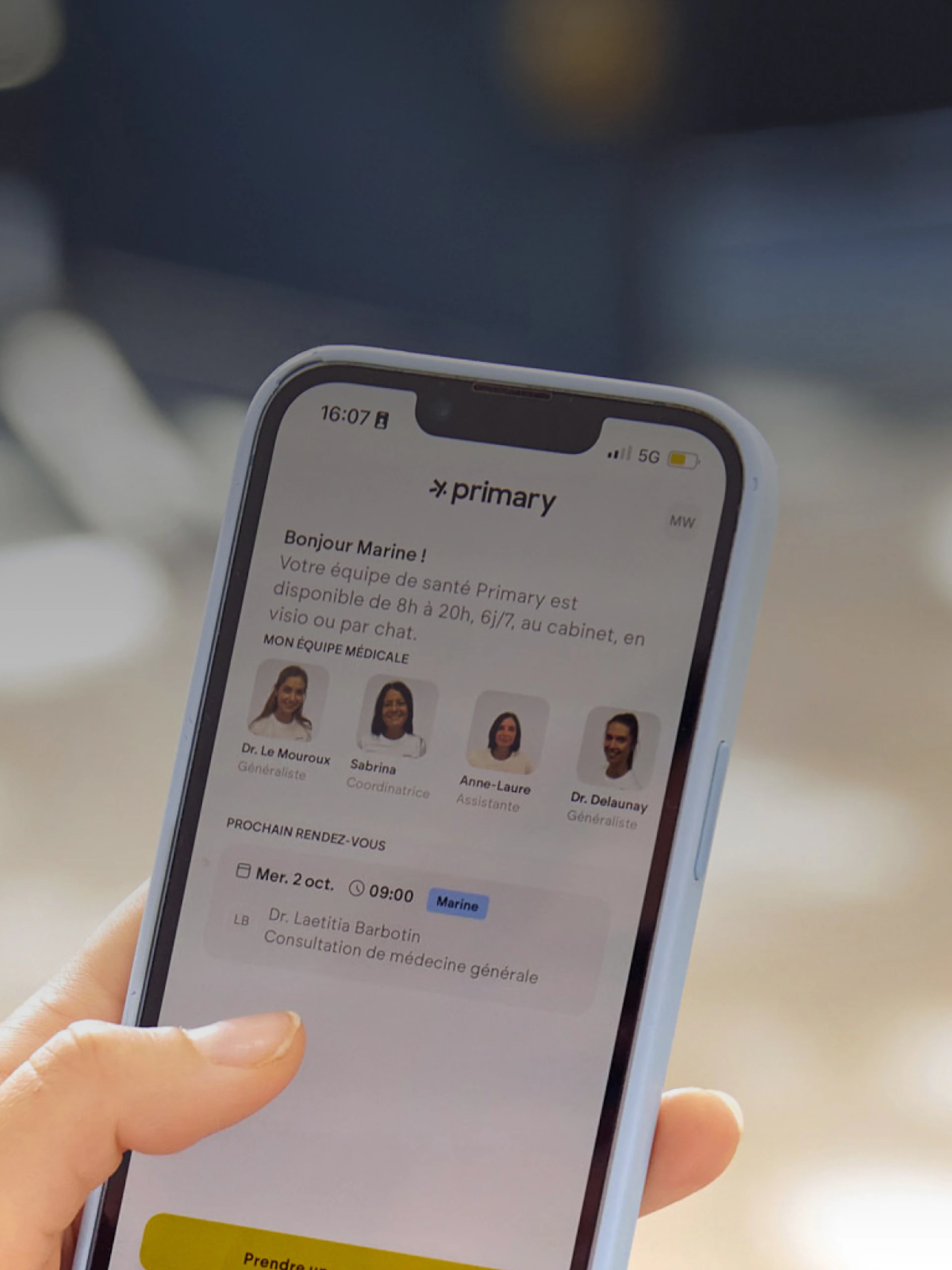 A photographic close-up of a hand holding a smartphone displaying the Primary app home screen