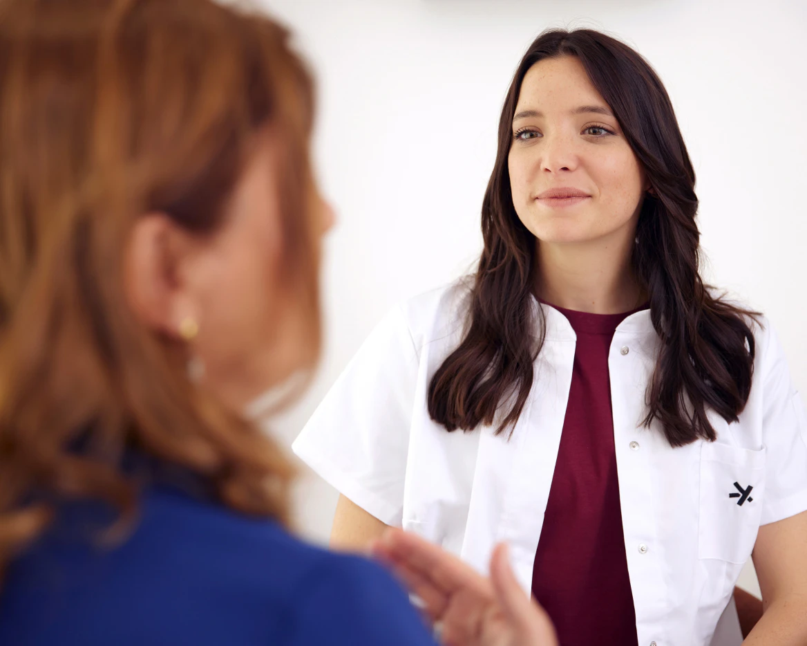 Preventative consultation at Primary: a warm exchange between a smiling female GP and her patient in her fifties (seen from behind).