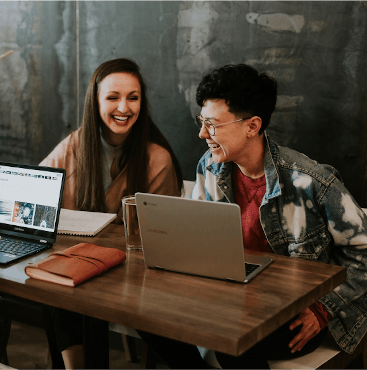 Two workers laughing in front of laptops