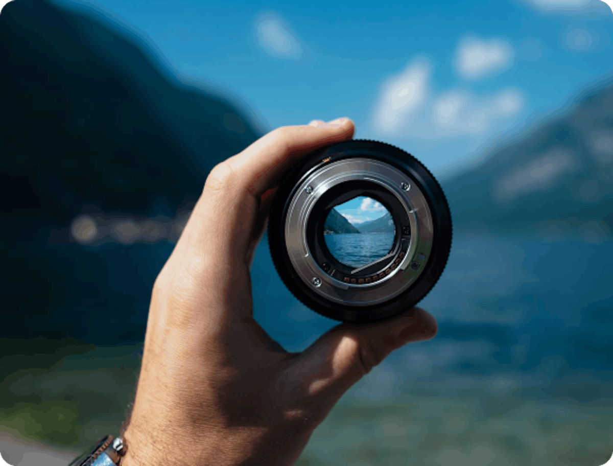 A camera lens held in front of mountains, demonstrating focus