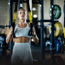Female in a gym, using TRX equipment to workout. 
