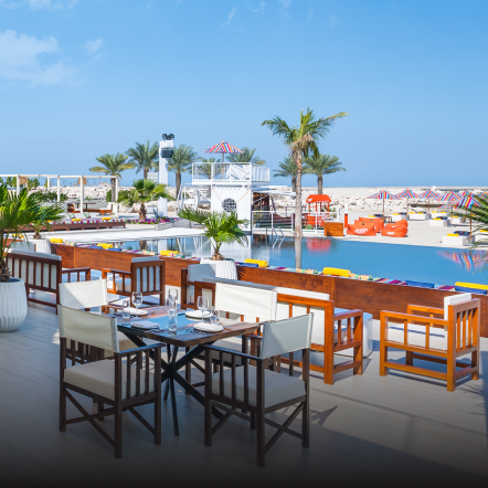 Restaurant with tables and chairs overlooking a scenic view of a pool and blue skies. 