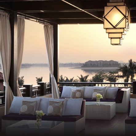 Shaded terrace with comfortable cushions and seating, with a sunset view in the background. 