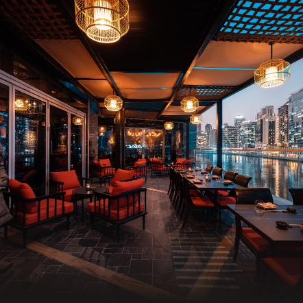 Dimly lit restaurant terrace overlooking a canal with skyscrapers in the background. 