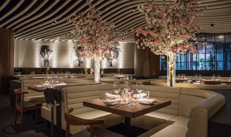 Indoor restaurant adorned with blossom flowers and art on the walls, with comfortable and spacious booths for guests to dine in. 