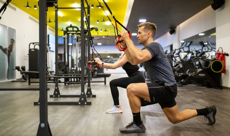 Male and female training in a quiet and bright gym using TRX equipment. 