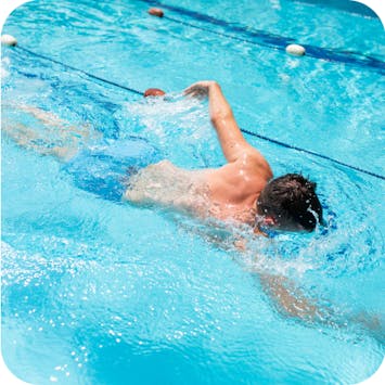 Male wearing blue swim shorts, swimming in a lap pool. 
