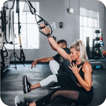 Female and male in a gym, using TRX equipment to workout. 