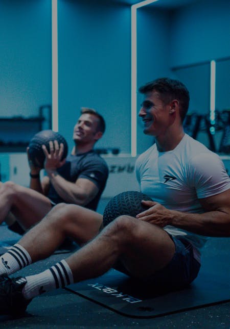 two men and two women training with crossfit ball in a gym studio with blue light