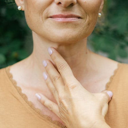 Detailansicht einer Frau, die sich mit der Hand an den Hals greift.