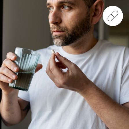Ein Mann, der gerade eine Kapsel einnimmt, mit einem Glas Wasser in der Hand.
