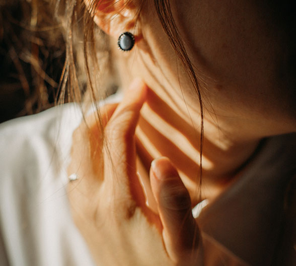 Detailaufnahme, eine junge Frau, die sich mit der Hand an den Hals fasst.