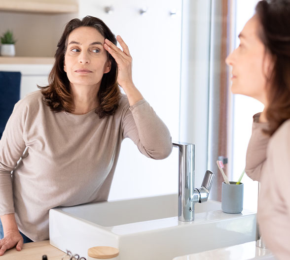 Eine ältere Dame, die im Spiegel ihr Gesicht begutachtet. 