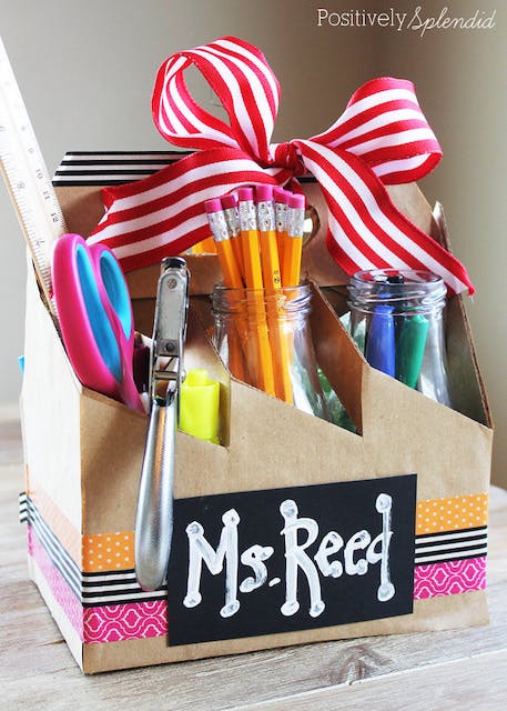 Cardboard supply kit with teacher's name written on the front and filled with pens and pencils. 