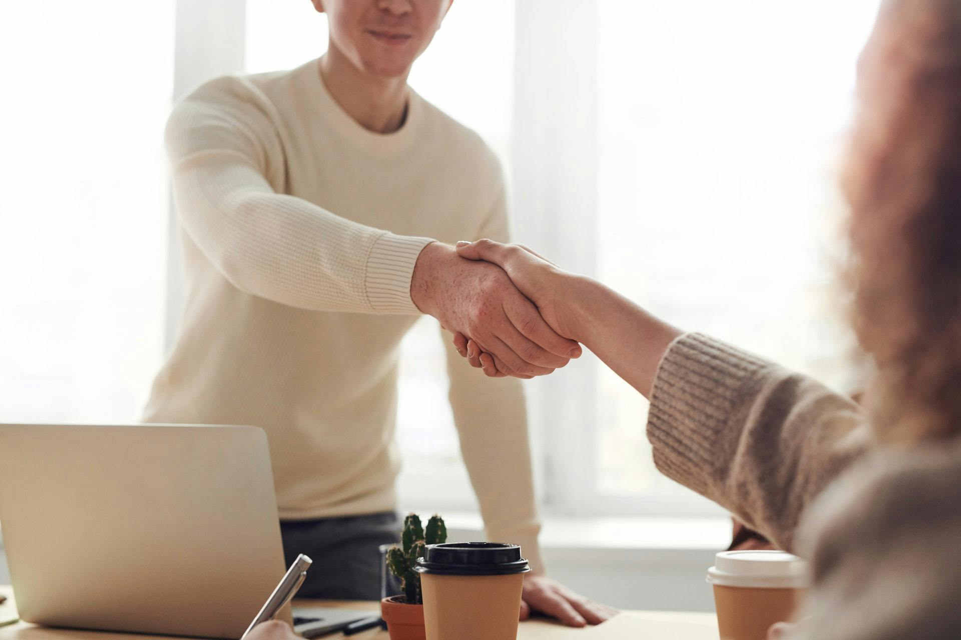 A teacher and a parent shake hands across a desk.