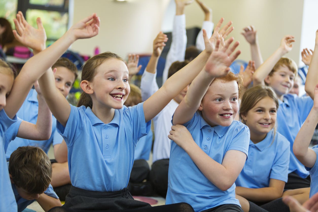 Excited students raise their hands to answer ice breaker questions for kids in their classroom