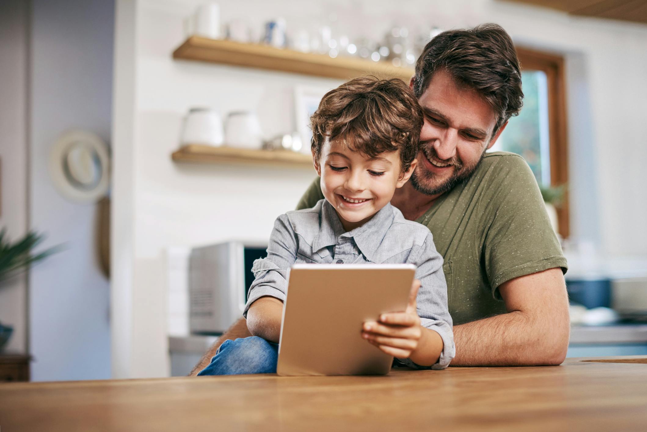 Photo of father sitting with his son while using a digital tablet
