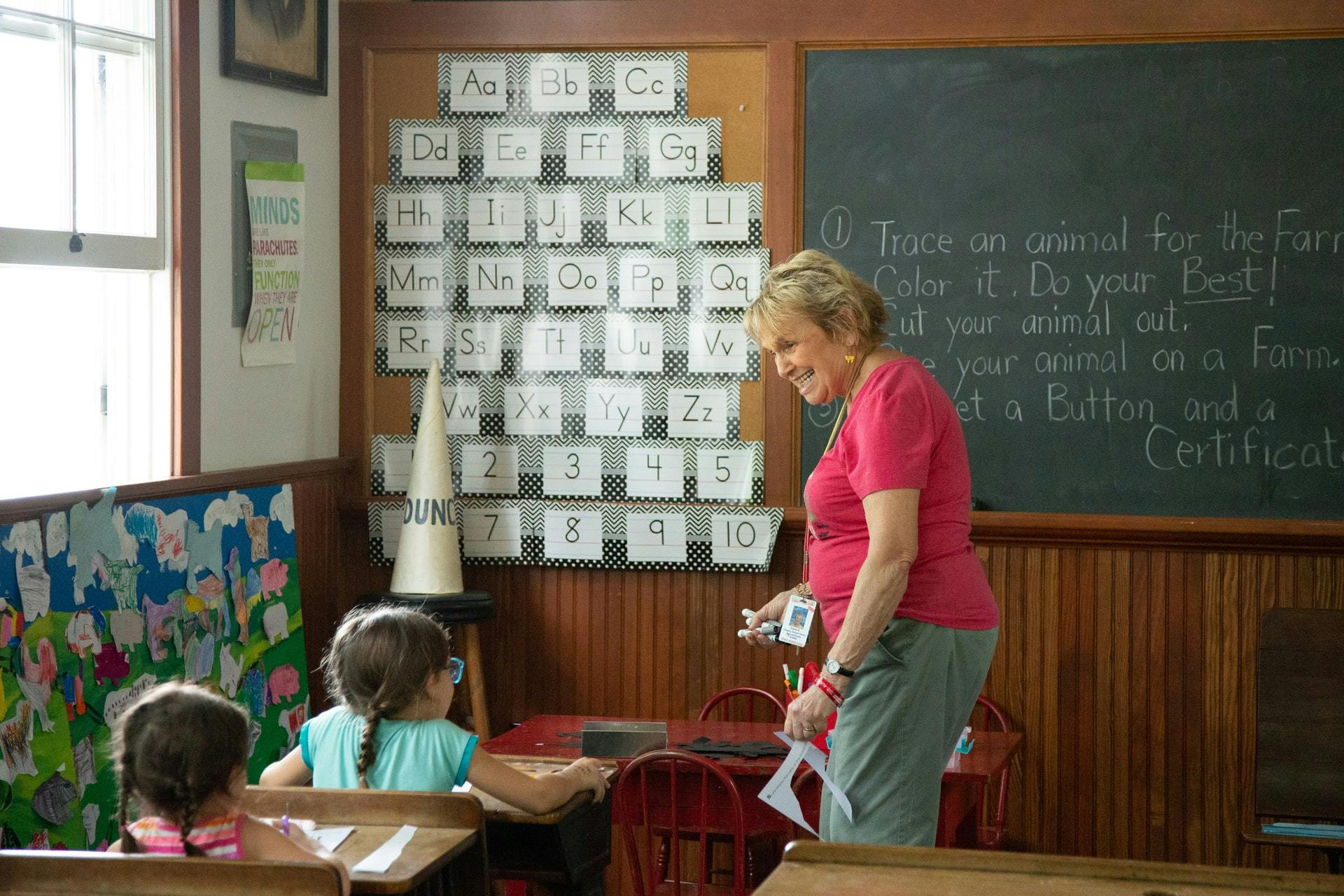 Elementary school teacher at the front of class smiling at a student in the front row.