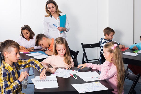 A teacher is standing and watching her students learning math