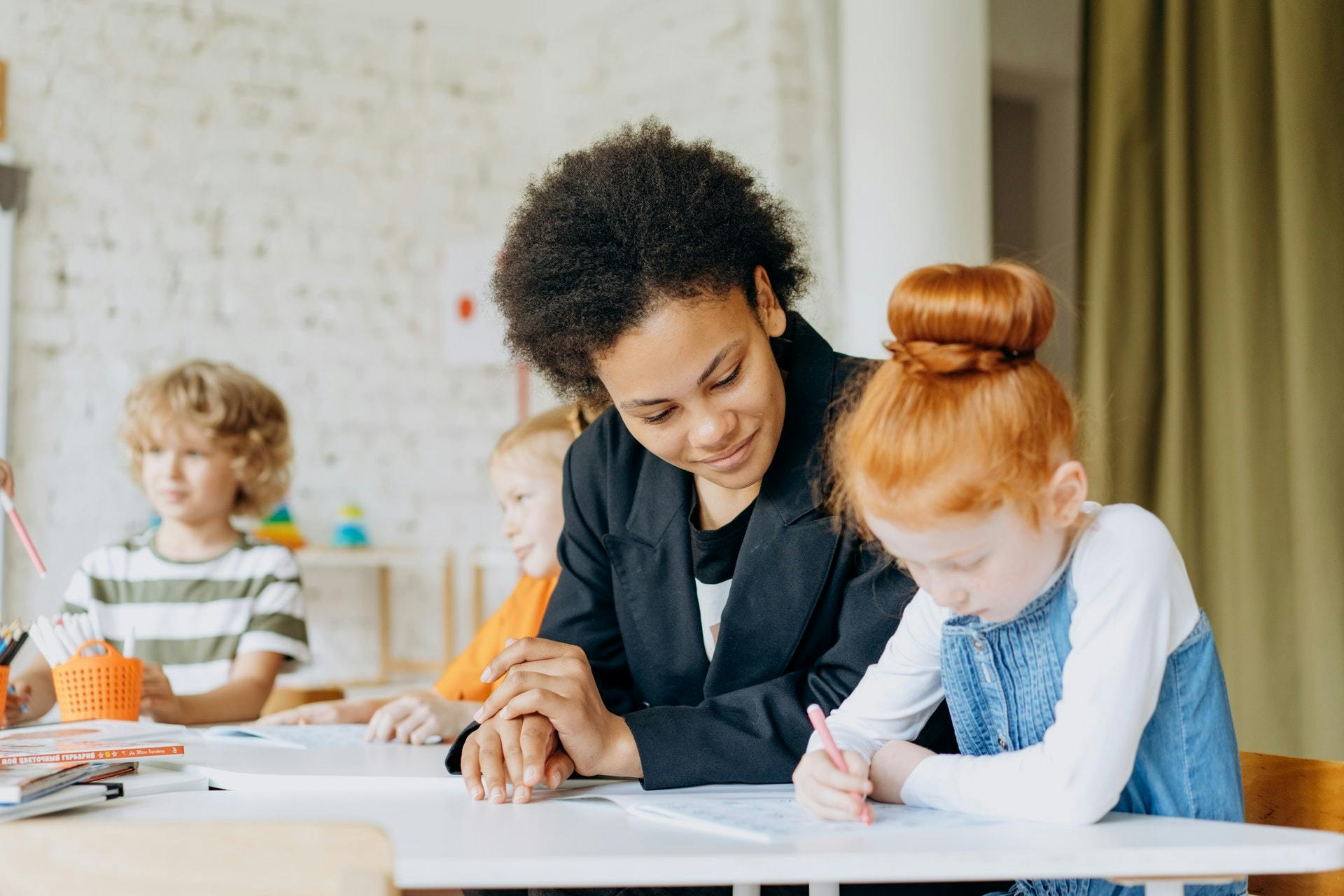 Teacher and child sit in the classroom and work on writing activities together.