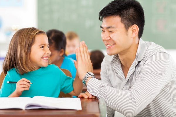 A teacher high-fives a student who's completed her work, which is one of his classroom management strategies to reward good behavior.