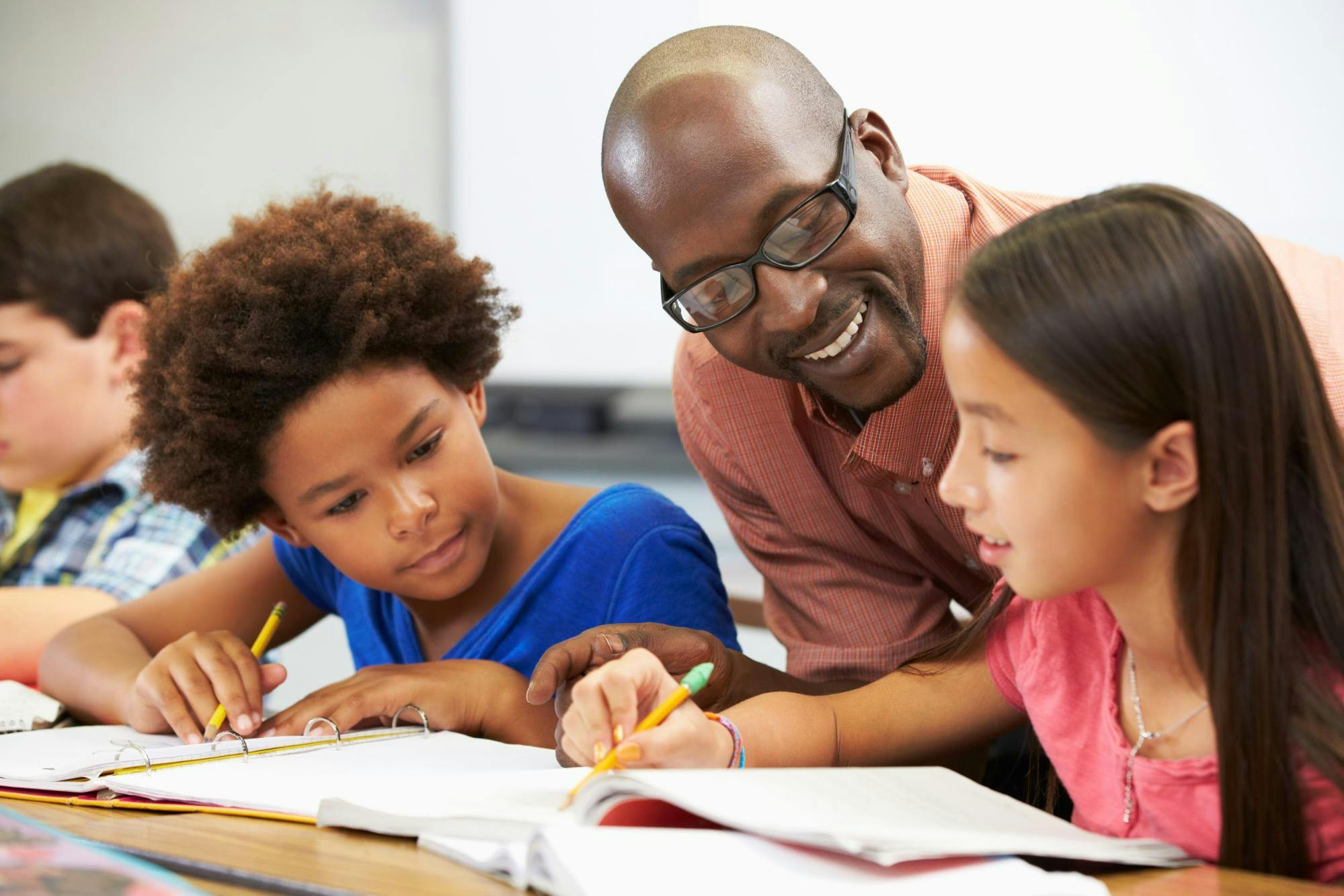 A teacher smiles at two young female students as they write in binders.