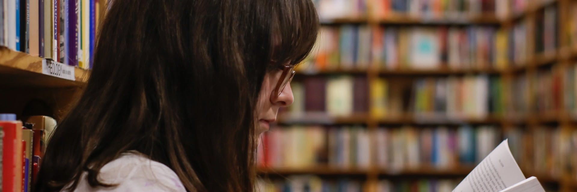 A female student reads a book in a school library and practices reading comprehension.