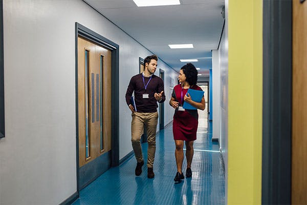 Two teachers walking together in hall.
